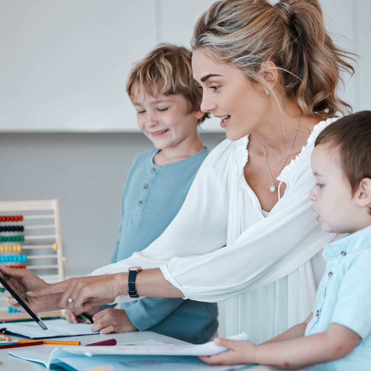 A candid, close-up view of a younger child from a Multi-age family drawing in a workbook, with an older sibling working nearby, in a calm, sunlit homeschool setting.